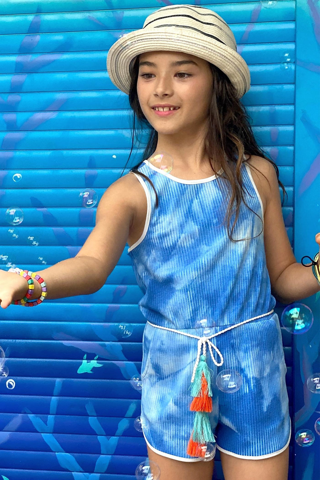 My hannah banana Girl’s Tie Dye Ribbed Knit Tassel Belt Romper.   Round Neckline & Sleeveless Ribbed Knit Material  Contrast Solid Trim Outline  Cloud or Water Tie Dye   A Minimal Boho Tassel Belt Semi Curved Sporty Short  Spring & Summer Beach Vacation Ready   Imported